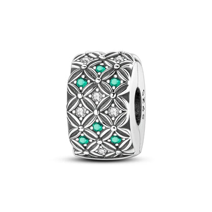 Silver charm with green gemstones and clear stones on a white background