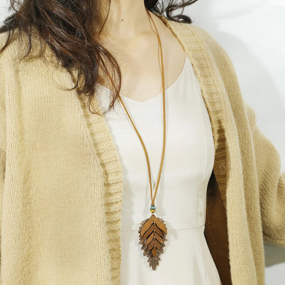 Person wearing a beige cardigan and white top with a long necklace featuring a leaf-shaped pendant.