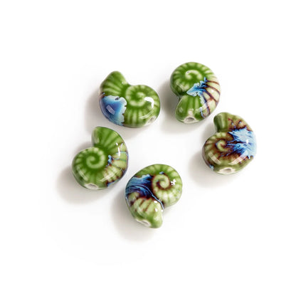 Five glossy ceramic nautilus shell beads with green, blue, and brown spiral patterns, arranged on a plain white background.