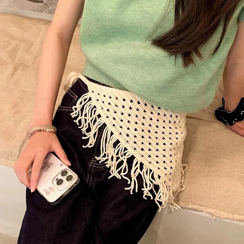 Person wearing a green top and black pants with a white crochet shawl, holding a phone.
