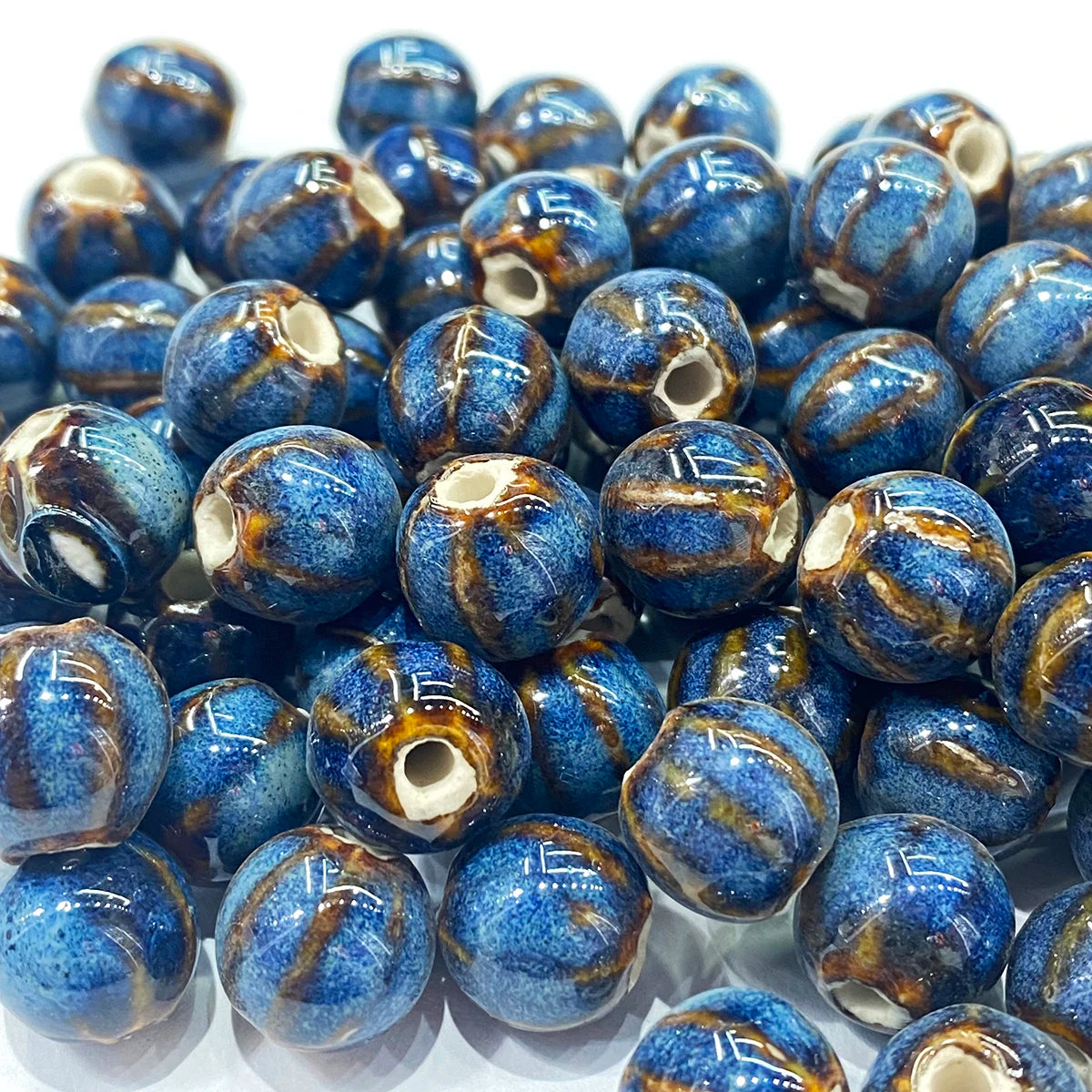 A pile of round, glossy blue glass beads with brown and gold marbled veins and a small white opening in the center.