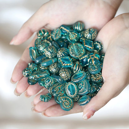 Hand holding a collection of decorative teal beads with gold accents on a neutral background