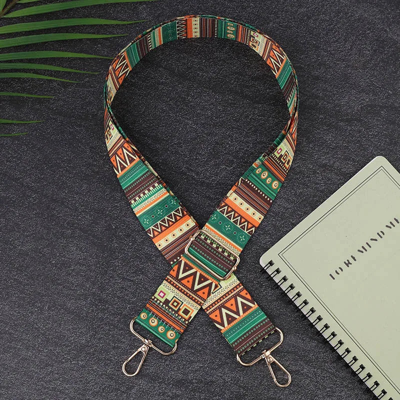 Colorful patterned strap with metal hooks on a dark surface with a notebook.