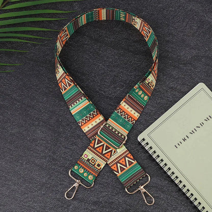 Colorful patterned strap with metal hooks on a dark surface with a notebook.