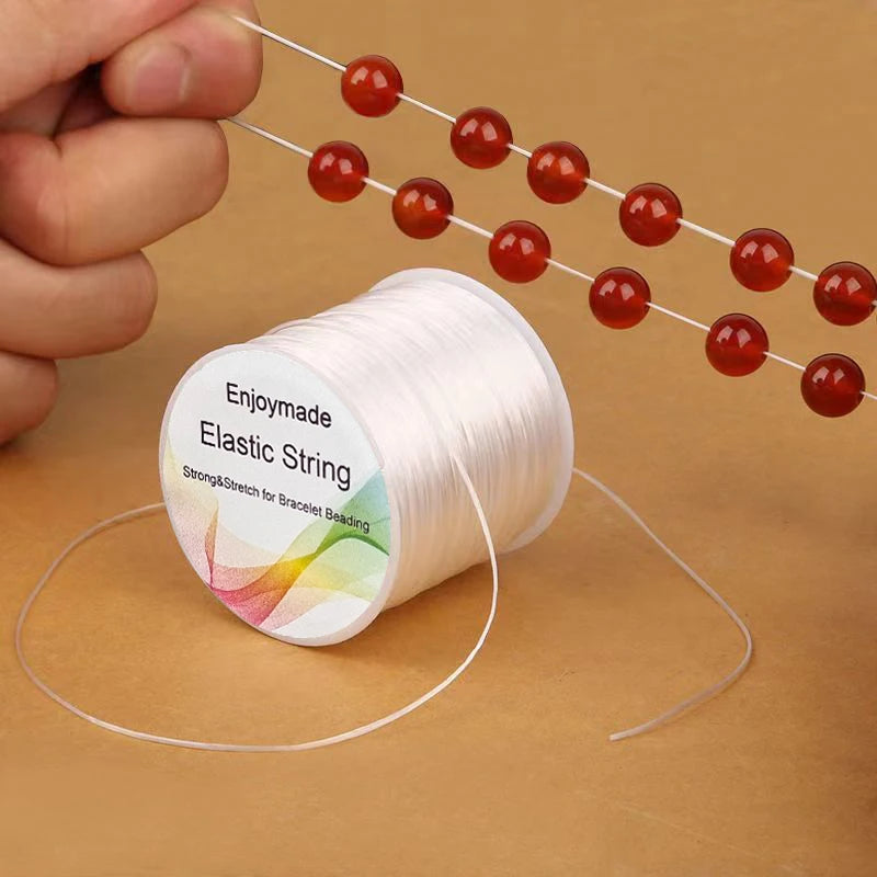 Spool of Enjoymade elastic string with red beads on a beige background