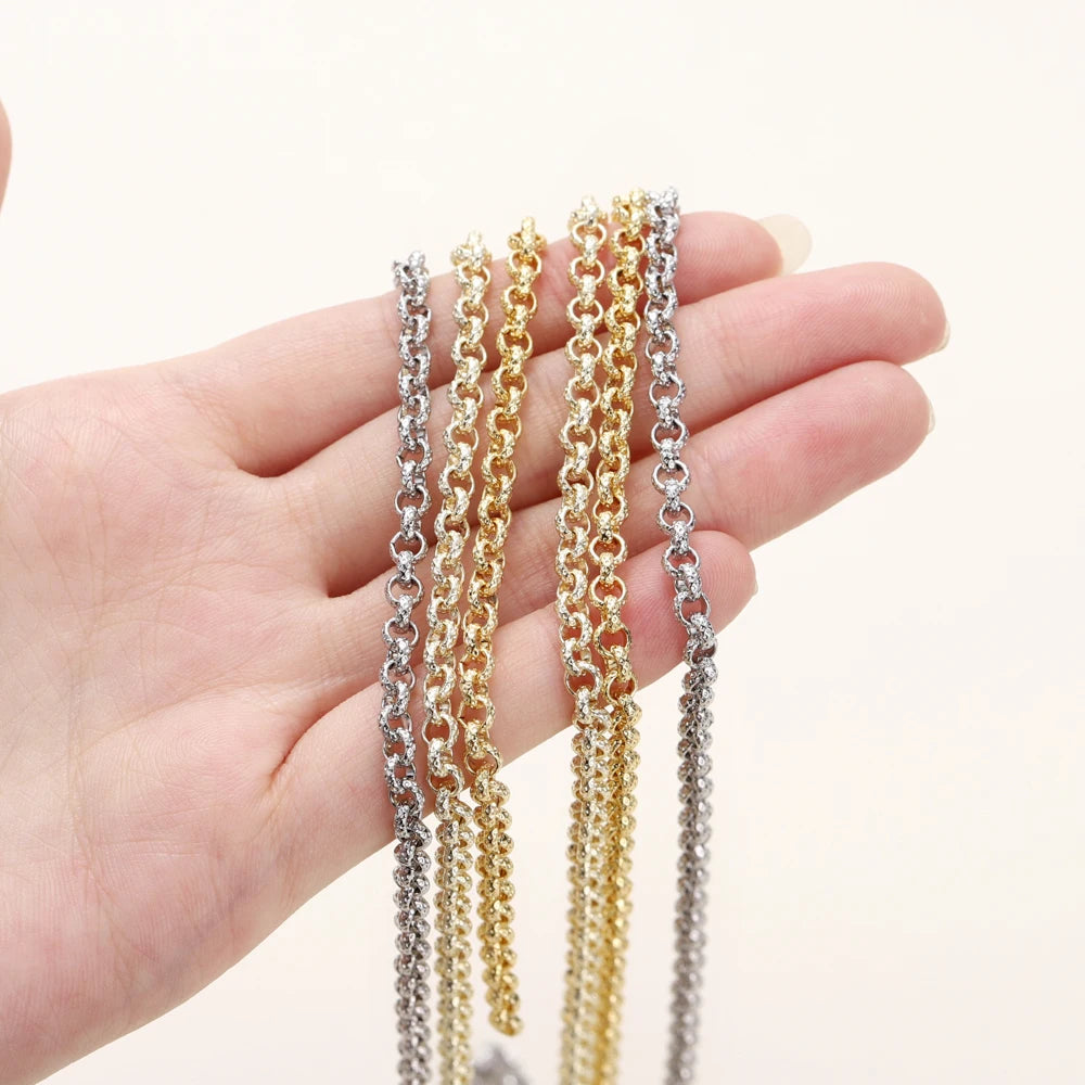 Three chains in silver and gold tones draped over a person's hand against a plain light background.