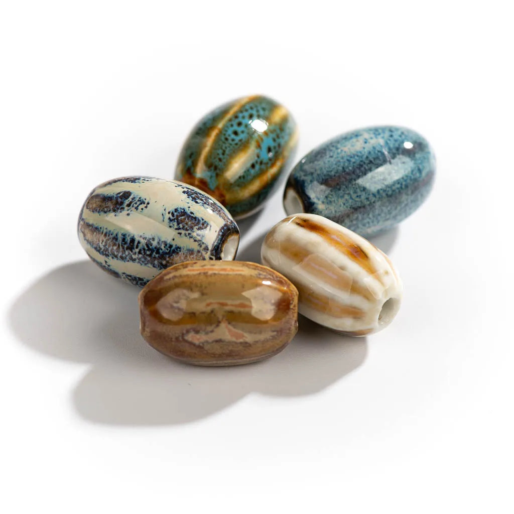 Five handmade ceramic beads with various marbled patterns in blue, brown, cream, and gold, arranged on a white background with soft shadows.