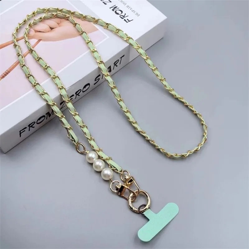 Gold chain with a pearl charm and green 'T' pendant on a gray surface.