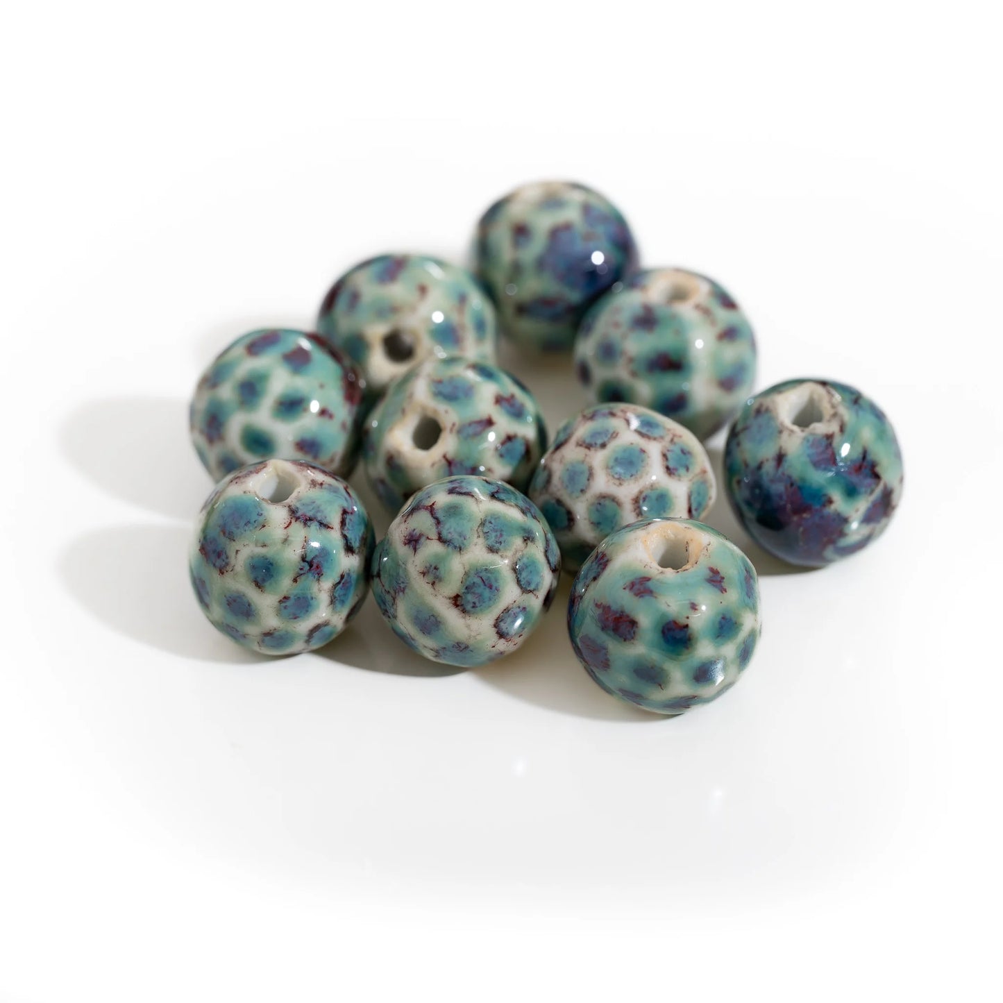 A cluster of handmade ceramic beads with a speckled pattern of teal blue, dark purple, and cream on a white background.