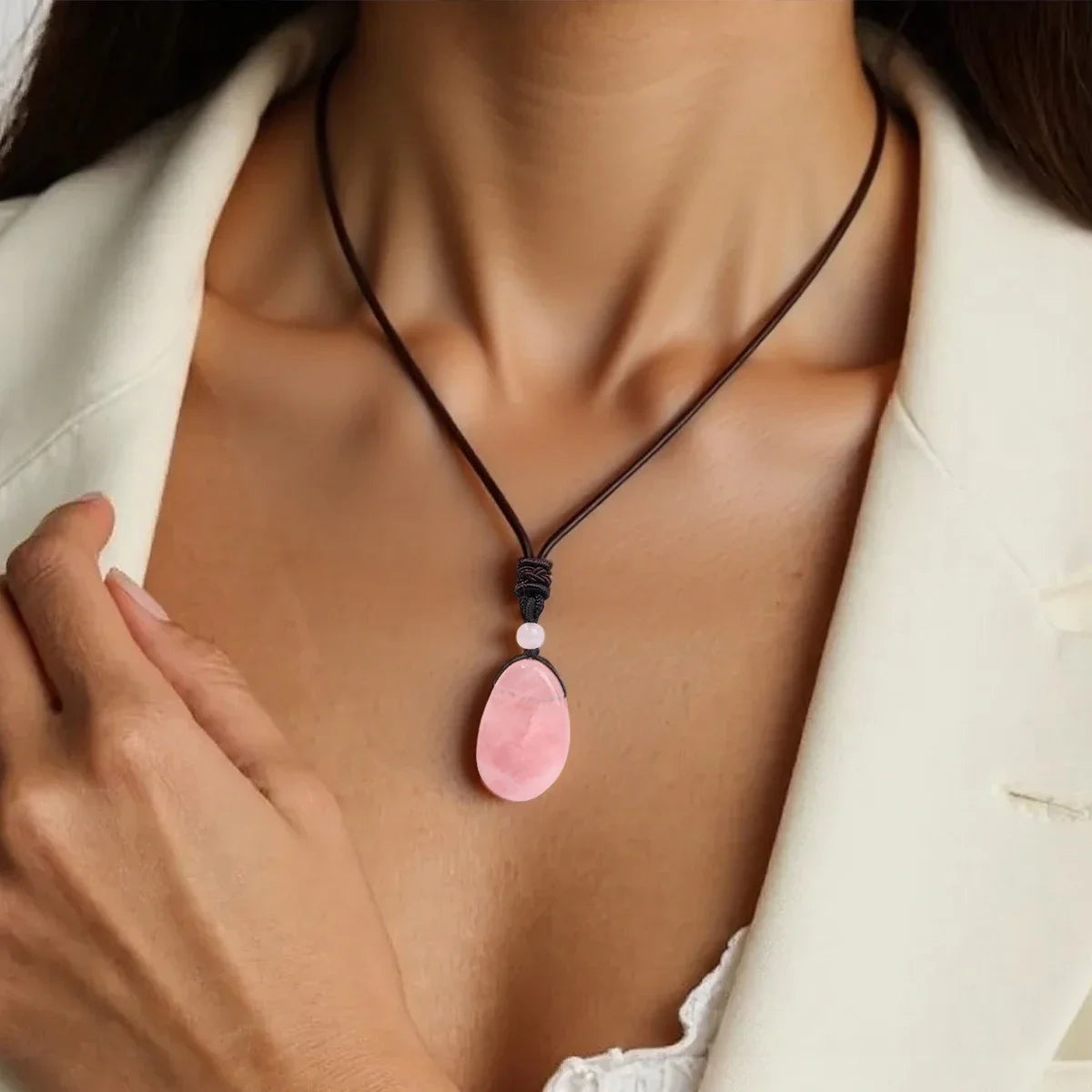 Necklace with a pink pendant worn by a person in a white outfit.