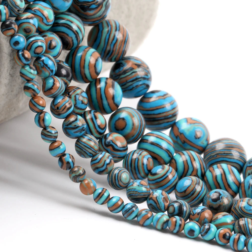 Multiple strands of round beads with a marbled pattern of turquoise blue, brown, black, and gray, draped over a light gray stone prop on a white background.