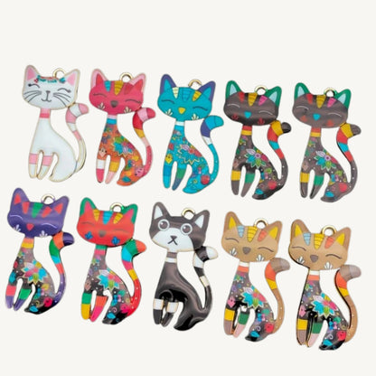 A set of 12 colorful cat-shaped charms or pendants arranged in two rows on a light cream background. Each cat has a different base color and a vibrant, multicolored paint-splatter pattern.