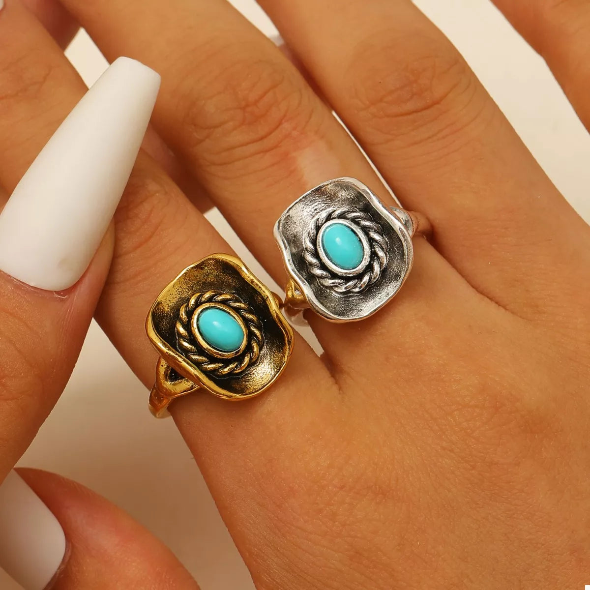 Two western rings with turquoise stones on a hand against a neutral background