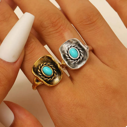 Two western rings with turquoise stones on a hand against a neutral background