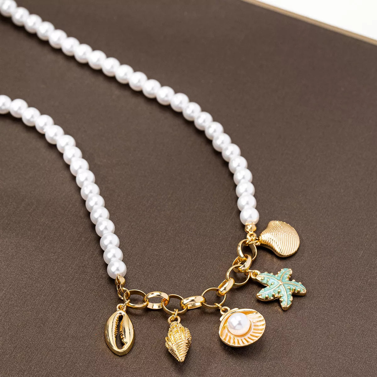 Pearl necklace with gold and green coastal charms on a brown surface