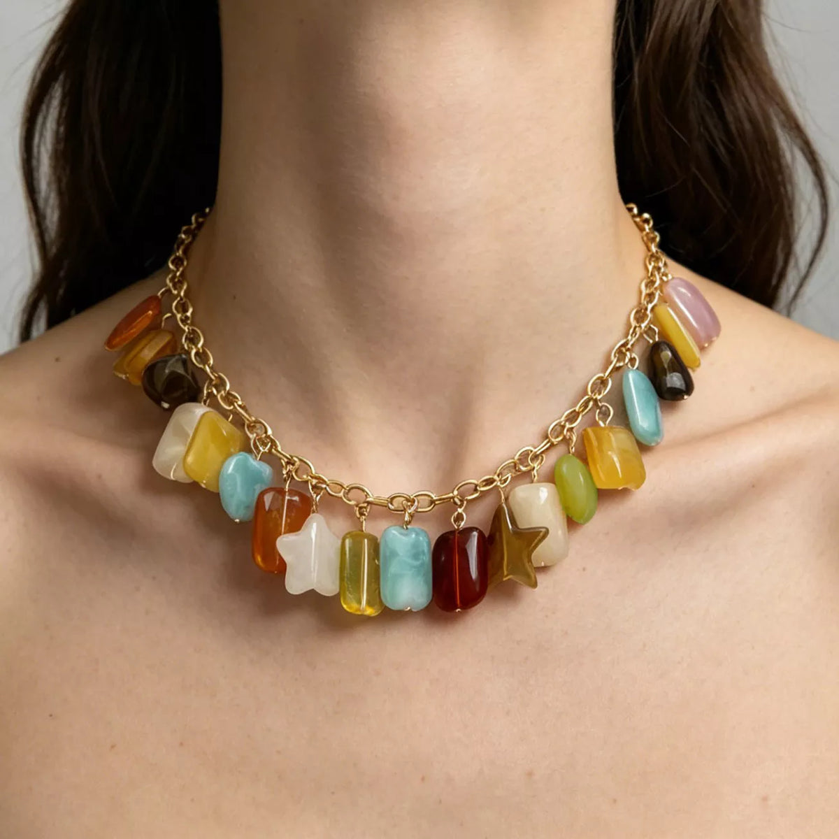 A gold chain necklace with dangling multicolored stone charms, shown worn on a model's neck. The charms include various stone shapes and colors such as yellow, blue, red, brown, and white.