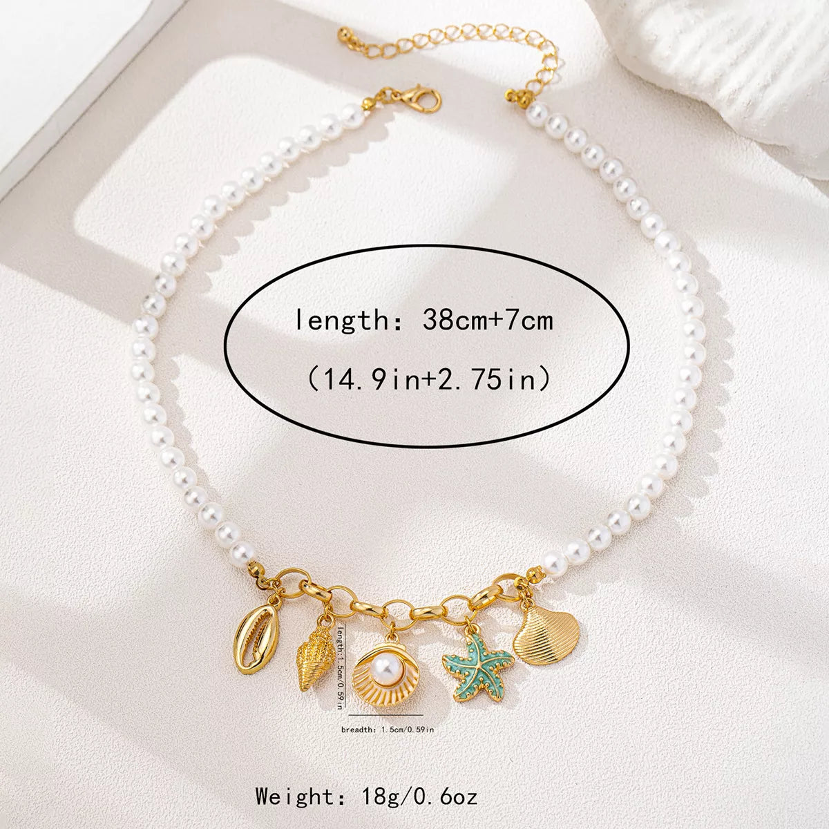 Pearl necklace with gold and green sea charms on a white surface, showing length and weight information.