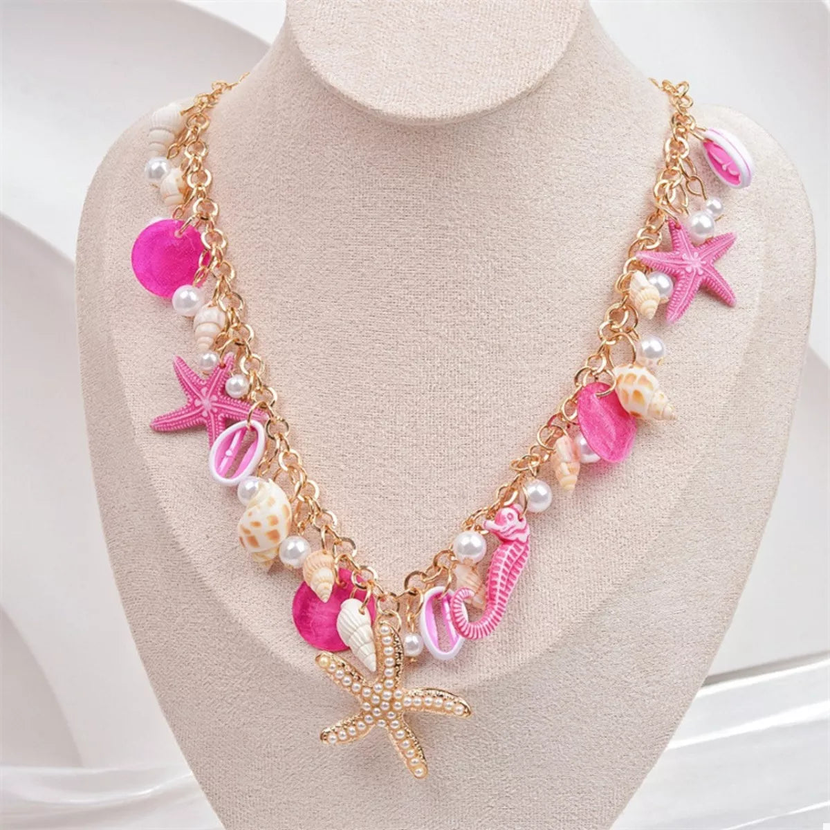 Necklace with pink and gold starfish and shell designs on a mannequin bust.