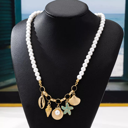Pearl necklace with gold and sea-themed charms on a black mannequin bust.